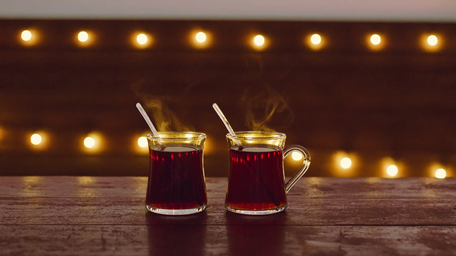 Two glasses of tea on a table at dusk, warm lights behind